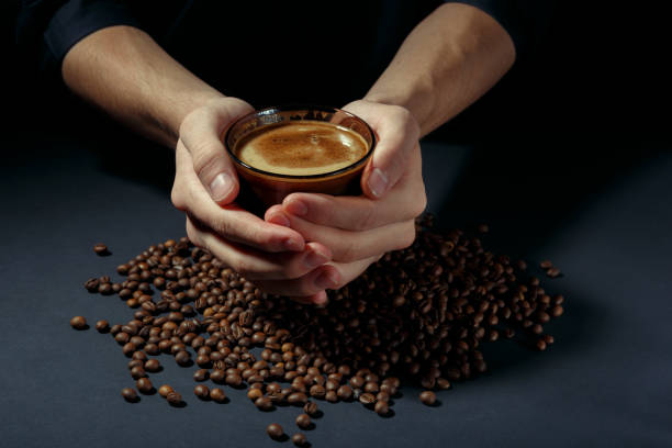 cup of hot coffee in the hands with scattered roasted grains on the table - fotografia de stock