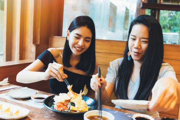 zwei junge attraktive asiatische frauen essen shrimp tempura japanisches essen im restaurant mit glück und freude - sushi japan restaurant food stock-fotos und bilder