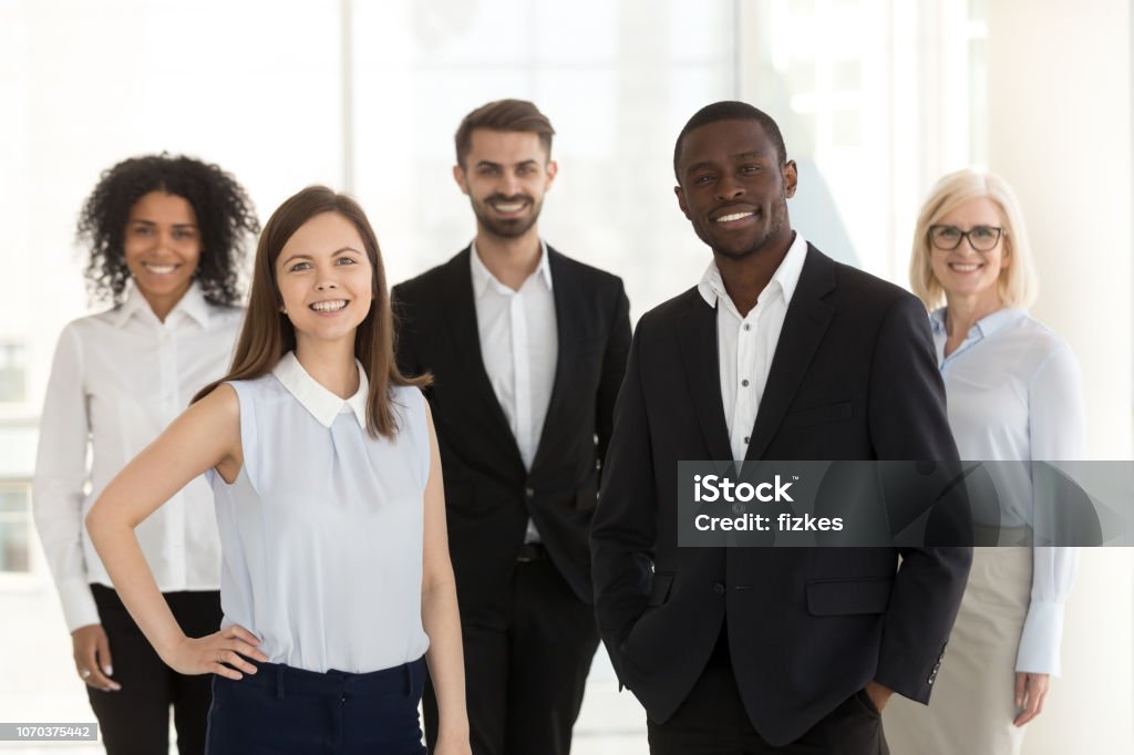 Portrait of smiling diverse work team standing posing in office Portrait of happy diverse work team standing looking at camera motivated for success and new achievements, smiling multiethnic managers or workers feel excited posing in office together Teamwork Stock Photo