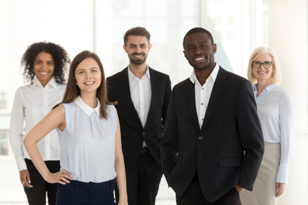 Portrait of smiling diverse work team standing posing in office Portrait of happy diverse work team standing looking at camera motivated for success and new achievements, smiling multiethnic managers or workers feel excited posing in office together organization photos stock pictures, royalty-free photos & images