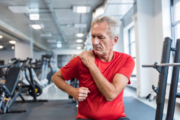 Senior man suffering from shoulder pain at rehabilitation center Senior man suffering from shoulder pain sitting at gym. Mature man feeling pain in his shoulder during workout at rehabilitation center. shoulder stock pictures, royalty-free photos & images