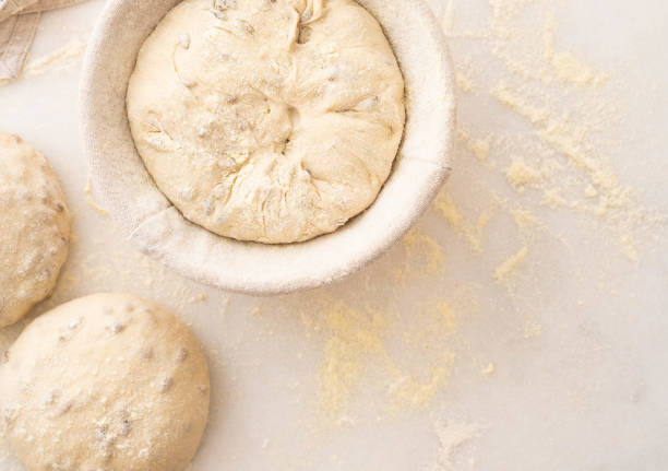Baking bread. Dough in proofing basket on table with flour, sunflower seeds. Top view. Baking bread. Dough in proofing basket on wooden table with flour. Top view. banneton bread proofing stock pictures, royalty-free photos & images