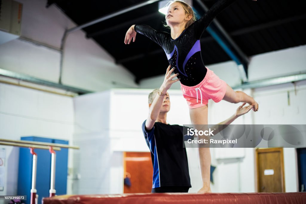 Coach training young gymnast to balance on a balance beam Gymnastics Stock Photo