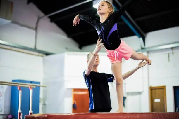 Photo of Coach training young gymnast to balance on a balance beam