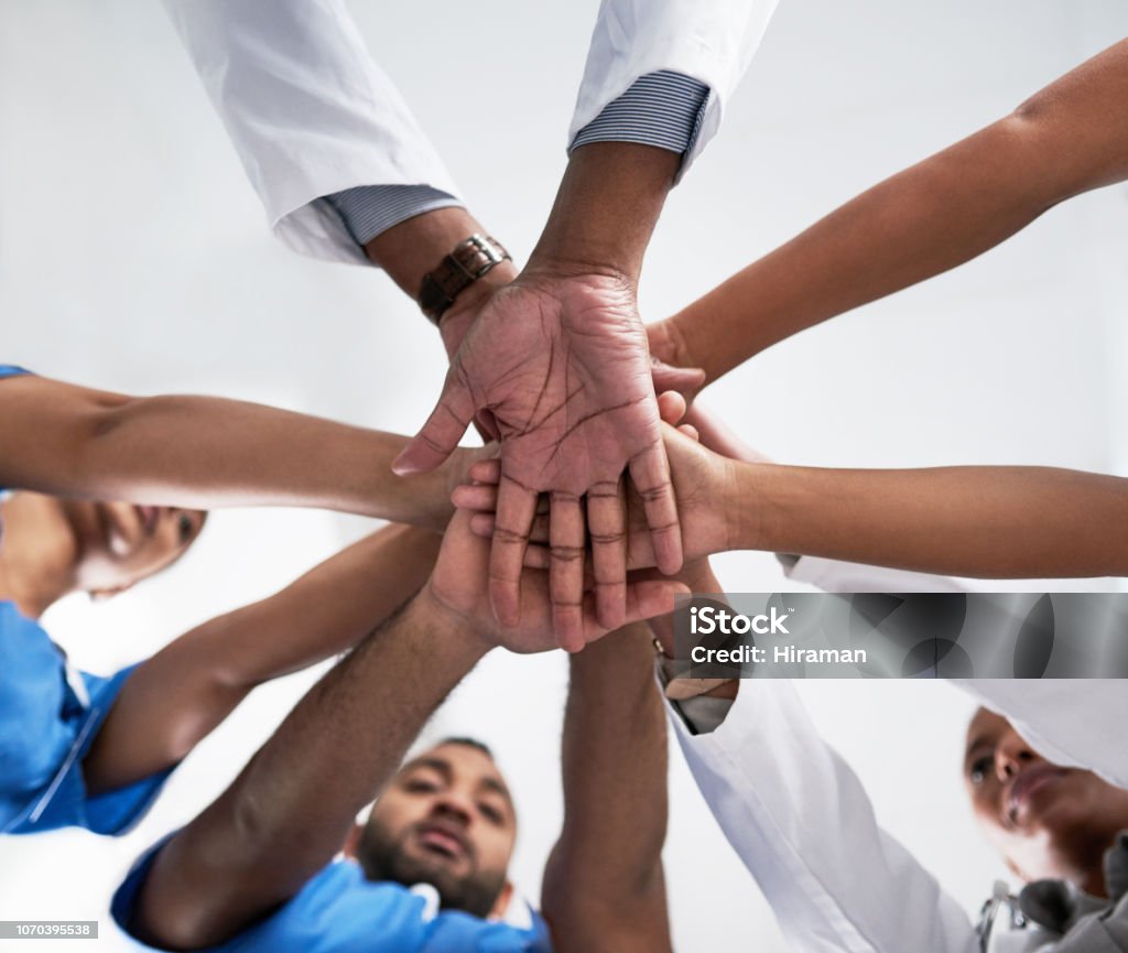 Teamwork allows us to perform at our best Low angle shot of a group of medical practitioners joining their hands together in a huddle Adult Stock Photo