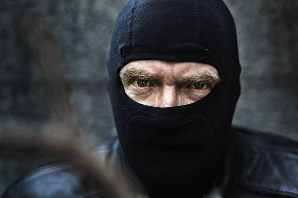 Scary man disguised by black balaclava glares threateningly at camera.