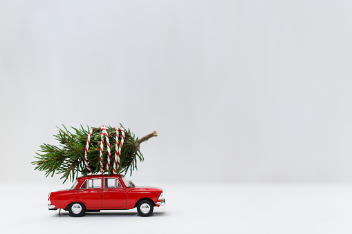 Red toy car with a christmas tree on the roof, garland bokeh on the background, shallow depth of field.