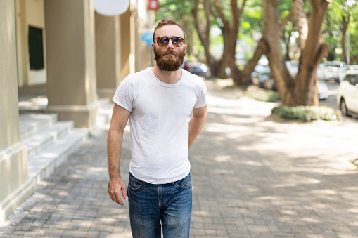 Focused handsome hipster guy enjoying weekend or vacation. Young man in sunglasses walking down summer street . walking outdoors concept