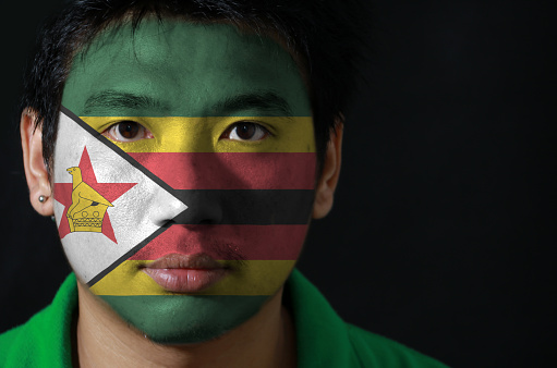 Portrait of a man with the flag of the Zimbabwe painted on his face on black background. The concept of sport or nationalism.