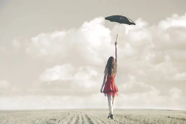 Photo of woman hides behind a black umbrella on a spring day on a green grass