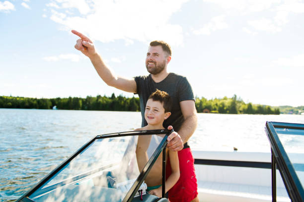 uomo alla guida di una barca in vacanza con il figlio - sailing nautical vessel family lake foto e immagini stock