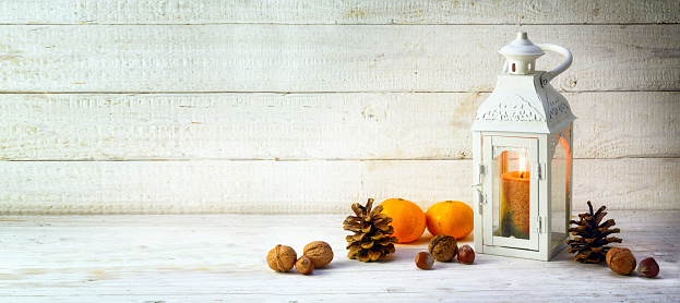 candle light lantern with pine cones, nuts and tangerines as christmas decoration on a wide, bright wooden background, panoramic format with large copy space, selected focus, narrow depth of field