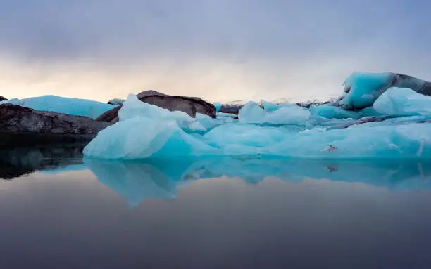 Blue icebergs floating in the Glacier Lagoon (Jökulsarlon), Iceland. Icebergs are reflected in the water and have a very beautiful natural blue colour. Clouds are dark, it is sunset time.