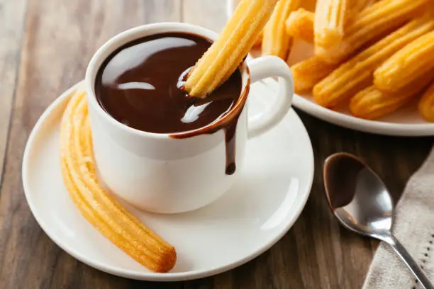 Traditional spanish churros with hot chocolate sauce on a rustic wooden table