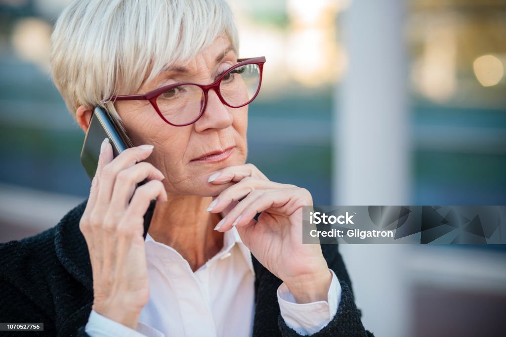 Worried mature businesswoman talking on the mobile phone, resting her arm on chin Worried mature businesswoman talking on the mobile phone, resting her arm on chin. Work anywhere concept. Using Phone Stock Photo