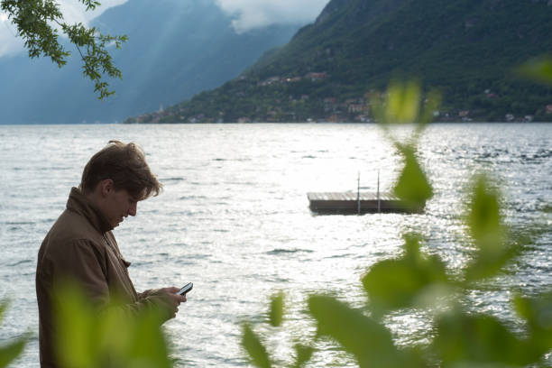 istock Young man uses cell phone on lake in mountains 1070538164