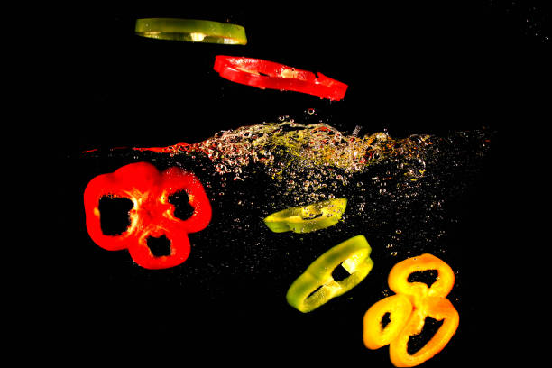 istock Red yellow and green peppers fall into water, on black background 1070543324