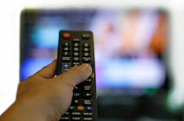 Hand with remote control and blurred TV set in the background