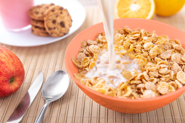 Breakfast pouring milk into corn flakes creating splash apple and orange fruit cookies stock photo