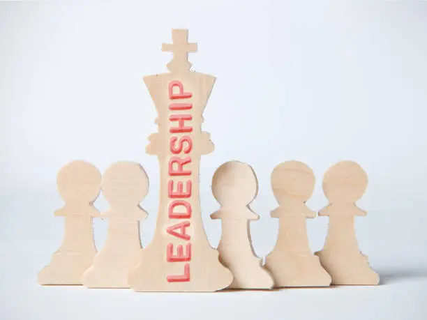 Chess figures, king and pawns with LEADERSHIP concept word imprinted on wooden surface