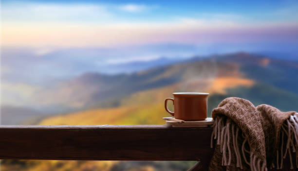 Hot cup of tea or coffee on the wooden railing on the mountains background. stock photo