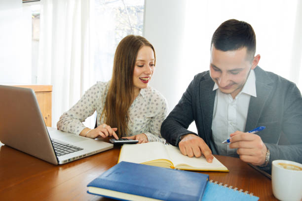 Couple Having A Business Cooperation Attractive Young Business Long Haired Woman Having Conversation With Her Coleague While Sitting At The Office Desk With Laptop. They Are Making Some Business Plans And Calculating. Cosigner in a Student Loan stock pictures, royalty-free photos & images