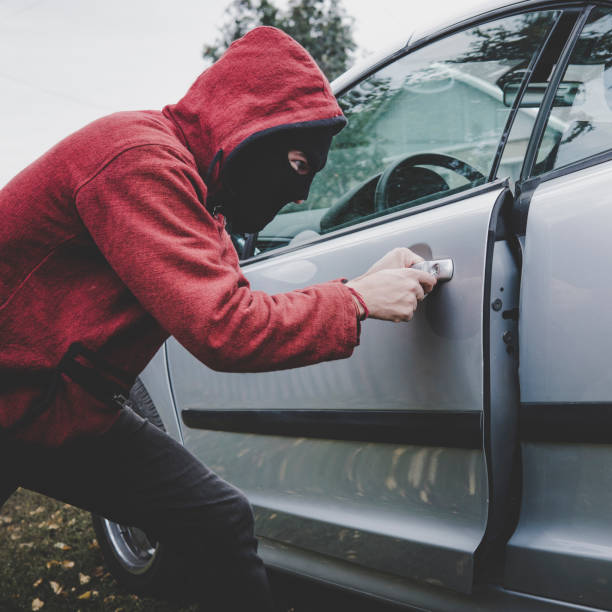 istock Young thief managed to break the car door using sceleton key. Evil-doer in black mask and hoodie unlocked the vehicle and got access to car cabin. Drug addict with hidden face hacks the automobile 1070598140