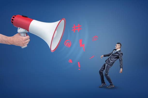 istock A giant hand holds a megaphone with exclamation signs falling out of it over a small businessman. 1070604868