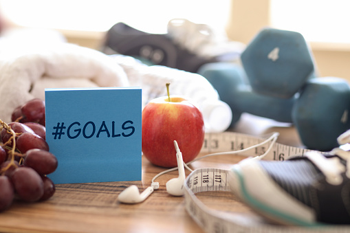 New year's resolution to get healthy in the coming year!  Group of objects includes:  #goals note, fruit, tape measure,ear buds, athletic shoes, dumbbells, water bottle and towel.   Concept of an individual preparing items for an exercise.