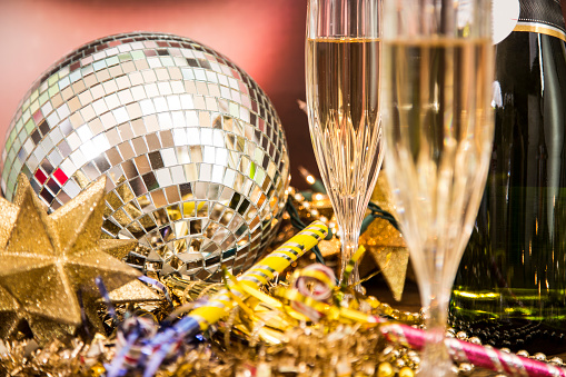 New Year's Eve celebration party with champagne, glasses, disco ball, decorations including: beads, lights, party horn blowers, and streamers.  Home party or nightclub setting.