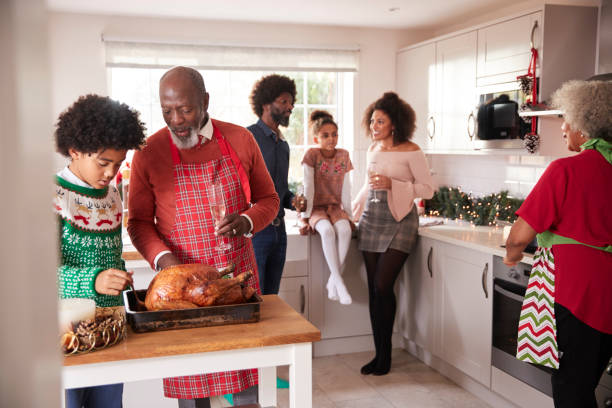 istock Mixed race, multi generation family gathered in kitchen before Christmas dinner, grandfather and grandson preparing roast turkey in foreground 1070626550