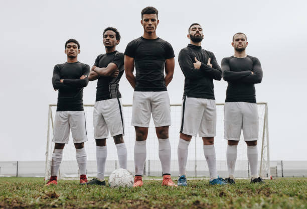 Footballers standing side by side on a soccer field Soccer players standing together with arms crossed on a soccer field. Low angle view of football players standing on soccer field during practice. football team stock pictures, royalty-free photos & images