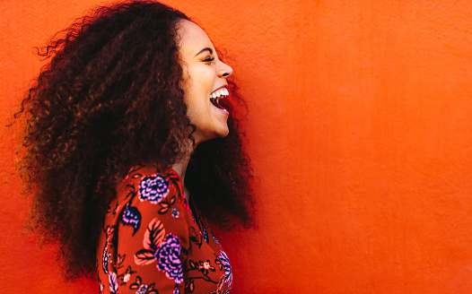 Side view of cheerful woman with curly hair standing against orange background. Close up of laughing african young woman.