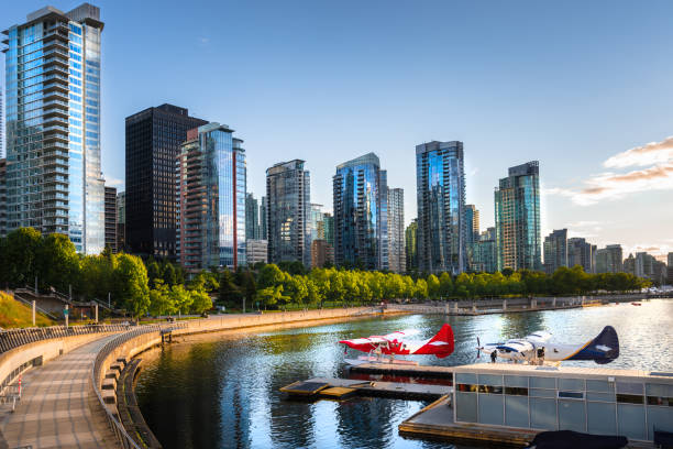 Downtown Vancouver Waterfront at Sunset Photo of Vancouver Waterfront at Sunset with High Rise Glass Buildings Lit by Warm Sunlight. Two Moored Seaplanes are in Foreground. Vancouver, BC, Canada. vancouver canada stock pictures, royalty-free photos & images