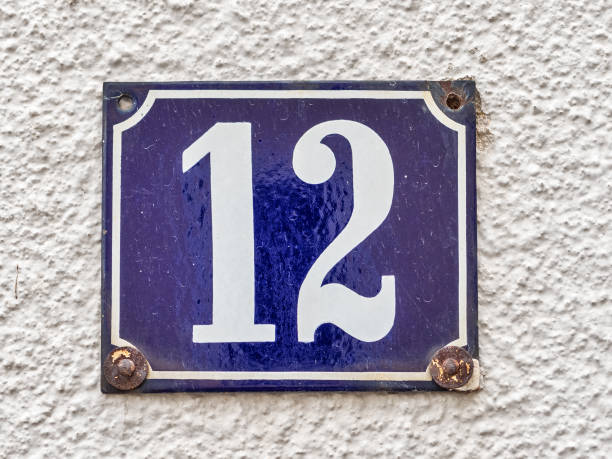 Wall of an old house in a little Bavarian town. House number 12. An old-fashioned rusty enamel sign. White number on dark blue background.