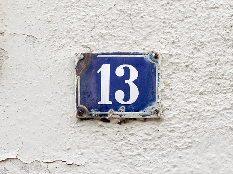 Wall of an old house in a little Bavarian town. House number 13. An old-fashioned rusty enamel sign. White number on dark blue background. Thirteen is a natural number and a prime number. In many countries it is seen as a unlucky number. In Italy it is a lucky number.