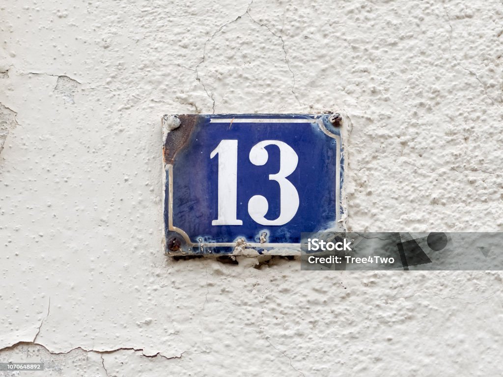 Old-fashioned enamel sign with house number 13 Wall of an old house in a little Bavarian town. House number 13. An old-fashioned rusty enamel sign. White number on dark blue background. Thirteen is a natural number and a prime number. In many countries it is seen as a unlucky number. In Italy it is a lucky number. Blue Stock Photo