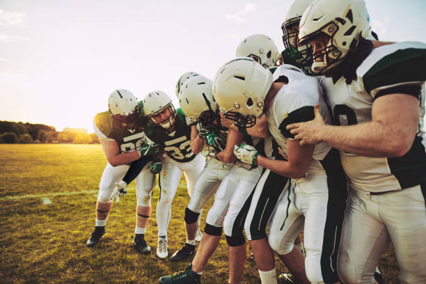 American football team having fun with their captain during practice Team of young American football players having fun trying to grab a football from their captain while standing on a sports field during a practice man laughing hard stock pictures, royalty-free photos & images