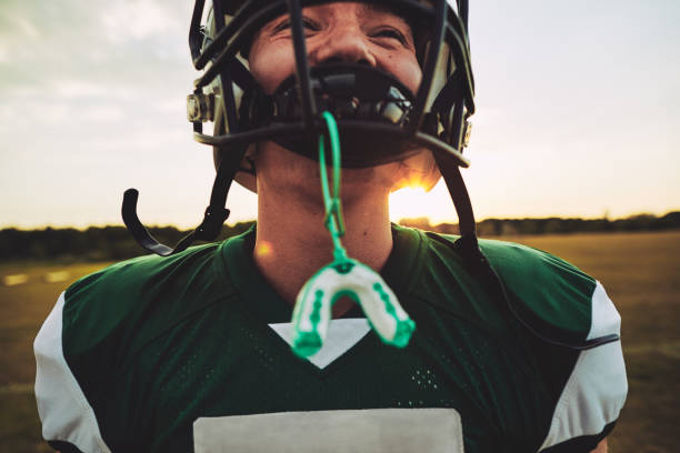 Young American football player standing on a field during practice Closeup of a young American football player with his mouthguard hanging from his helmet during a team practice session mouthguard stock pictures, royalty-free photos & images