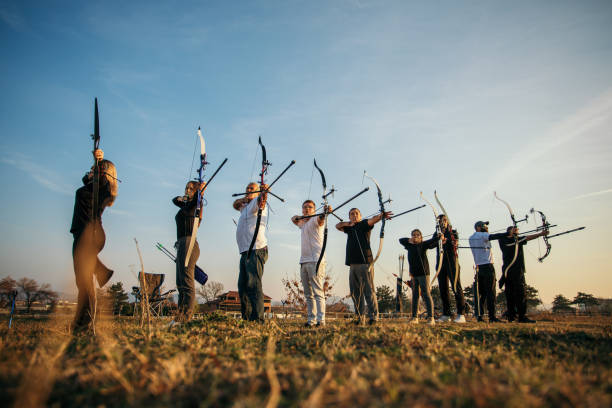 Group of people on archery training Large group of people on outdoors archery training at sunset. Theay are all aiming with bow and arrow. The group includes men, women, seniors, children, teenagers archery photos stock pictures, royalty-free photos & images