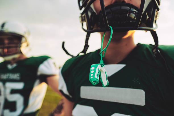 Young American football player with his mouthguard out during practice Closeup of a young American football player with his mouthguard hanging from his helmet during an afternoon practice mouthguard stock pictures, royalty-free photos & images