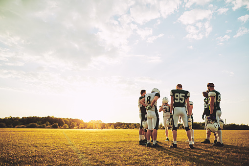 Group of young American football players standing together in a circle on a sports field talking strategy