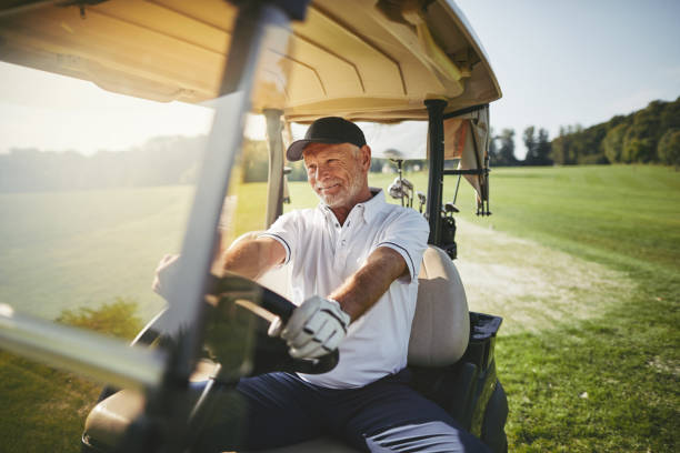 sorrindo sênior homem dirigindo seu carrinho de golfe em um fairway - golf cart golf mode of transport transportation - fotografias e filmes do acervo