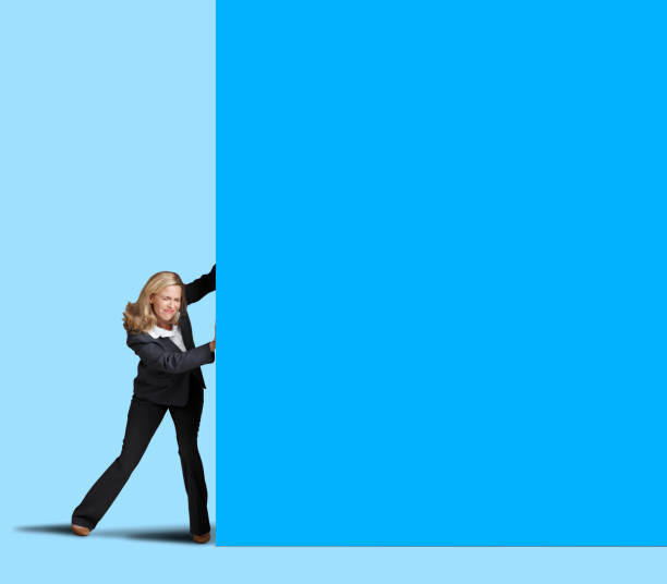 A businesswoman pushes against a large blue wall which provides ample room for copy and text.