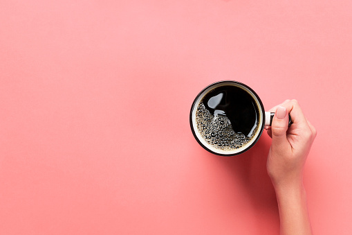 High angle of woman hands holding coffee mug on pink background Minimalistic style. Flat lay, top view isolated.
