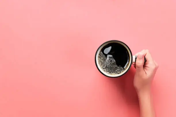 Photo of High angle of woman hands holding coffee mug on pink background Minimalistic style. Flat lay, top view isolated