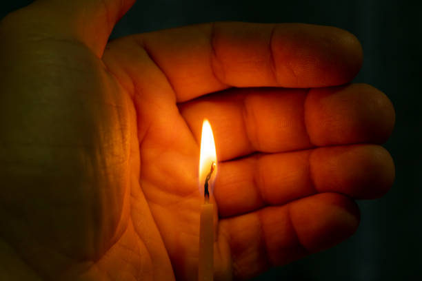 istock burning wax church candle in hand on black background 1070707986