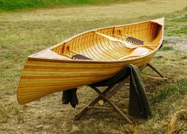 Wooden boat placed on a wooden stand in the meadow.After the boat and over the stand there is a blanket.In the boat there are two rowing boats and two knit benches.The boat is new.