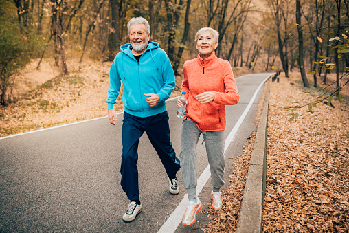 Fit senior couple jogging uphill in the autumn leaves covered park