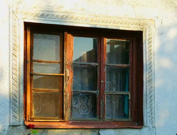 Old window with antique decor around. Lace and blue curtain as a reflection of life behind the window and red rose under the window.